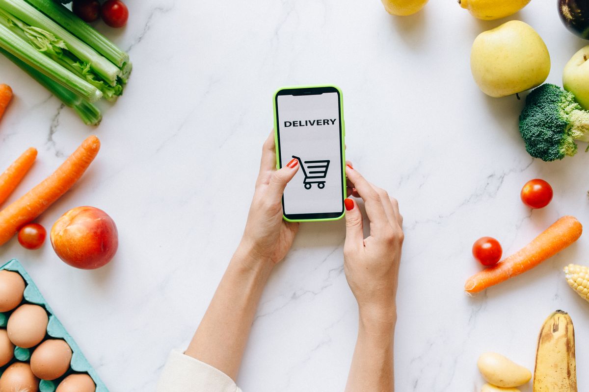 Person ordering grocery delivery on a smartphone surrounded by fresh food